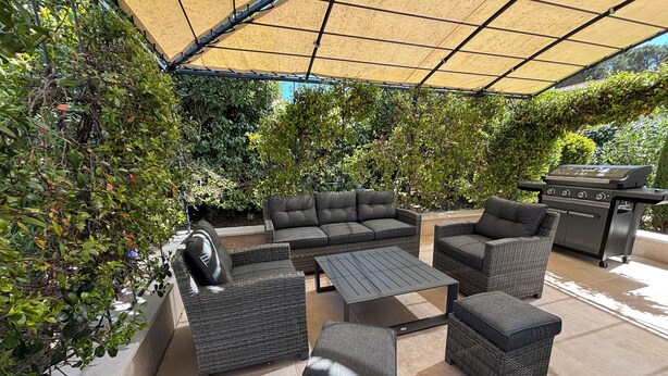 An outdoor patio with wicker furniture, a grill, and a shaded area.