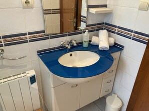 Une salle de bain avec un lavabo bleu, des meubles blancs, un miroir et un porte-serviettes.