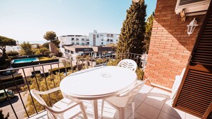 Een balkon met een witte tafel en stoelen, met uitzicht op een zwembad en gebouwen.