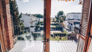 Een balkon met een houten vloer en metalen hekwerk, met uitzicht op een woonwijk met huizen en bomen.