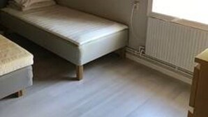 A small, single-bed room with a window, a radiator, and a partial view of a bed on the left.