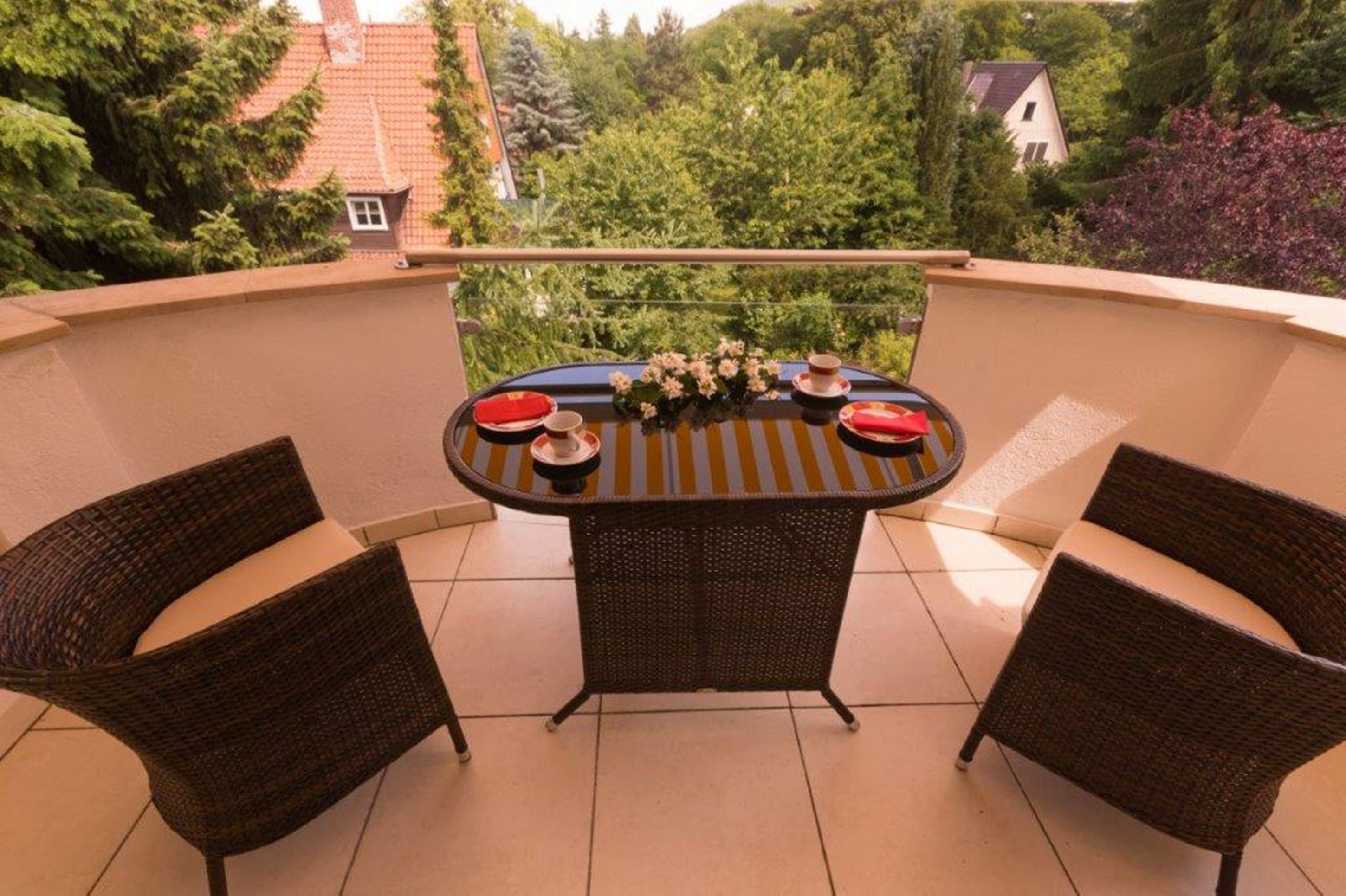 A balcony with a round table, two wicker chairs, and a view of greenery and buildings.