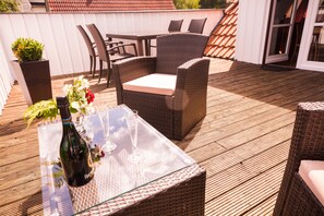 Een zithoek buiten met rieten meubels, een tafel, stoelen en een fles wijn.