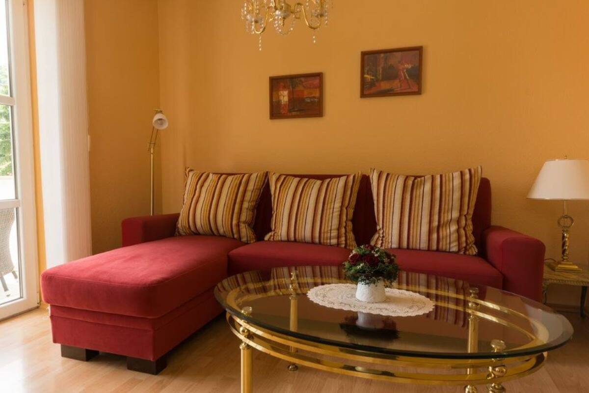 Un salon avec un canapé rouge, des coussins à rayures, une table basse en verre et deux tableaux accrochés au mur.