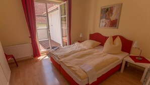 Ein Doppelbett mit rotem Kopfteil, ein Nachttisch mit Lampe sowie ein Bild an der Wand.