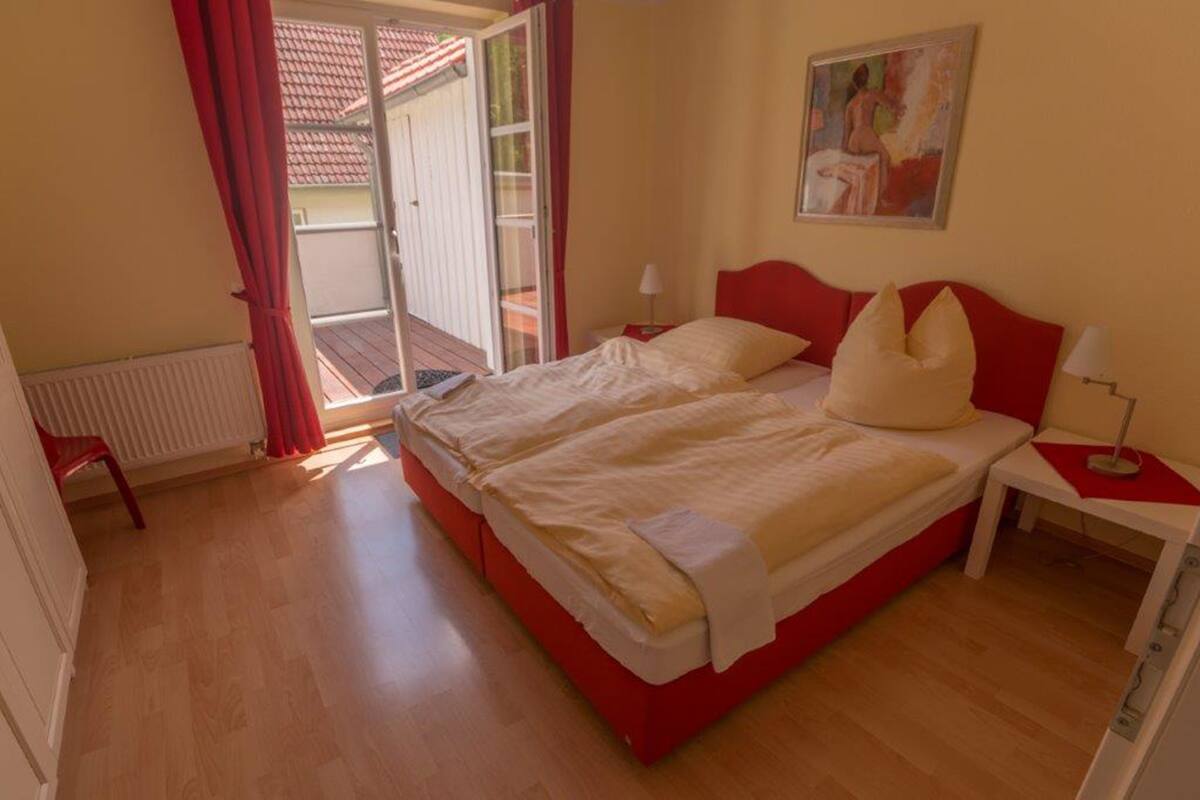 Un lit double avec une tête de lit rouge, une table de chevet avec une lampe et un tableau accroché au mur.