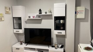 Uma sala de estar moderna com televisão de tela plana, armários brancos e uma prateleira com objetos decorativos.