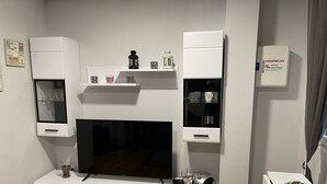 Uma sala de estar moderna com televisão de tela plana, armários brancos e uma mesa pequena com um prato decorativo.