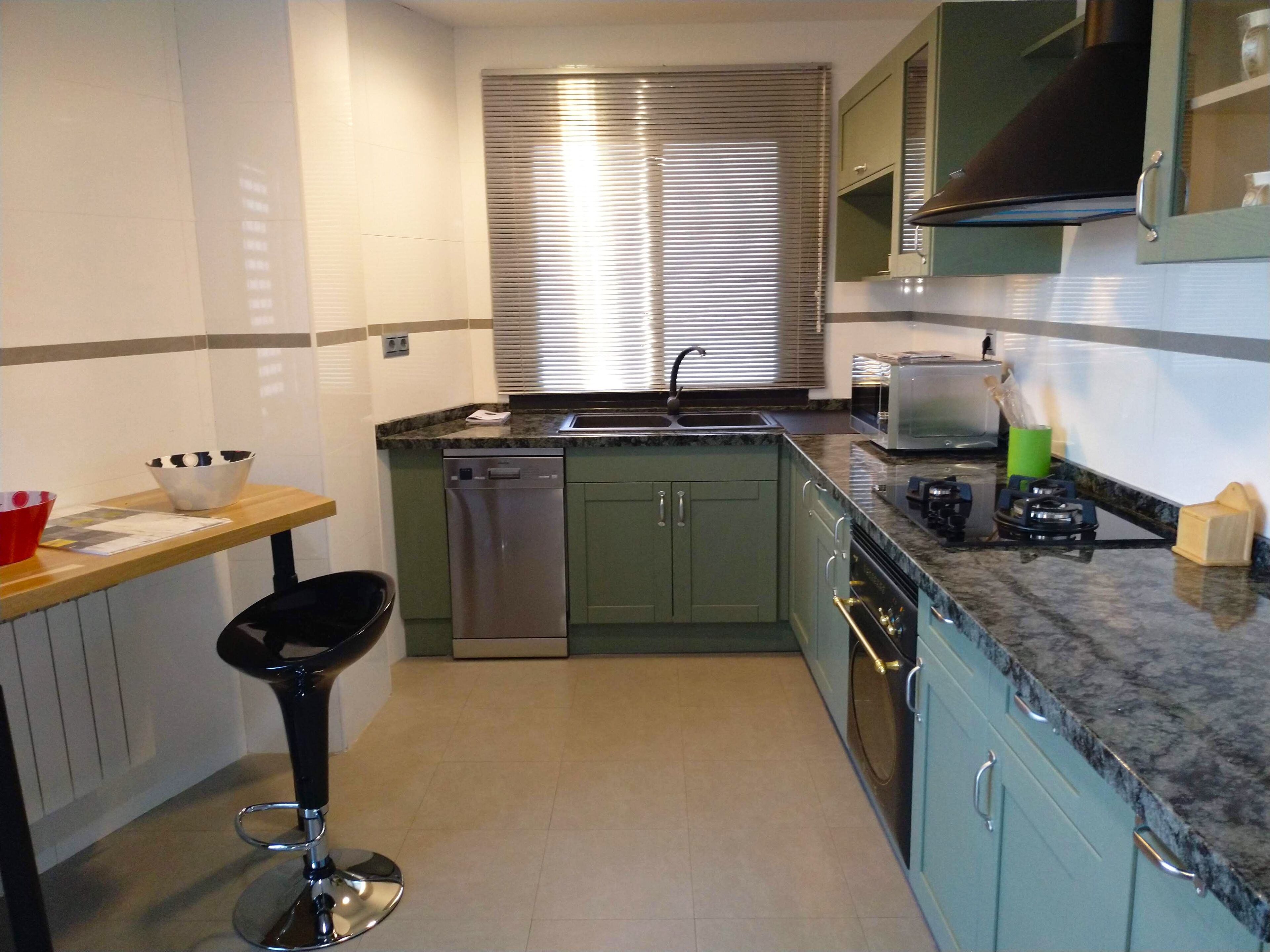 A compact kitchen with a dishwasher, a sink, a stove, and a bar stool.