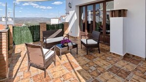 Una terraza con vistas, amueblada con sillas de mimbre y una mesa, y un dosel blanco.