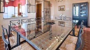 Un comedor con una mesa de vidrio, sillas de metal, una araña y un armario con puertas de vidrio.