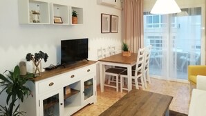 Una sala de estar moderna con televisor de pantalla plana, mesa de comedor de madera, sillas blancas y un ventanal con vista a la ciudad.