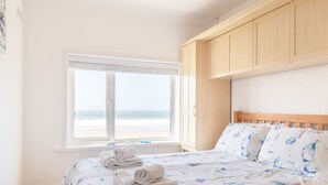 Ein Schlafzimmer mit einem Bett, einem Fenster mit Blick auf den Strand und Holzschränken.