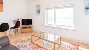 Ein modernes Wohnzimmer mit großem Fenster, Flachbildfernseher und Glastisch.