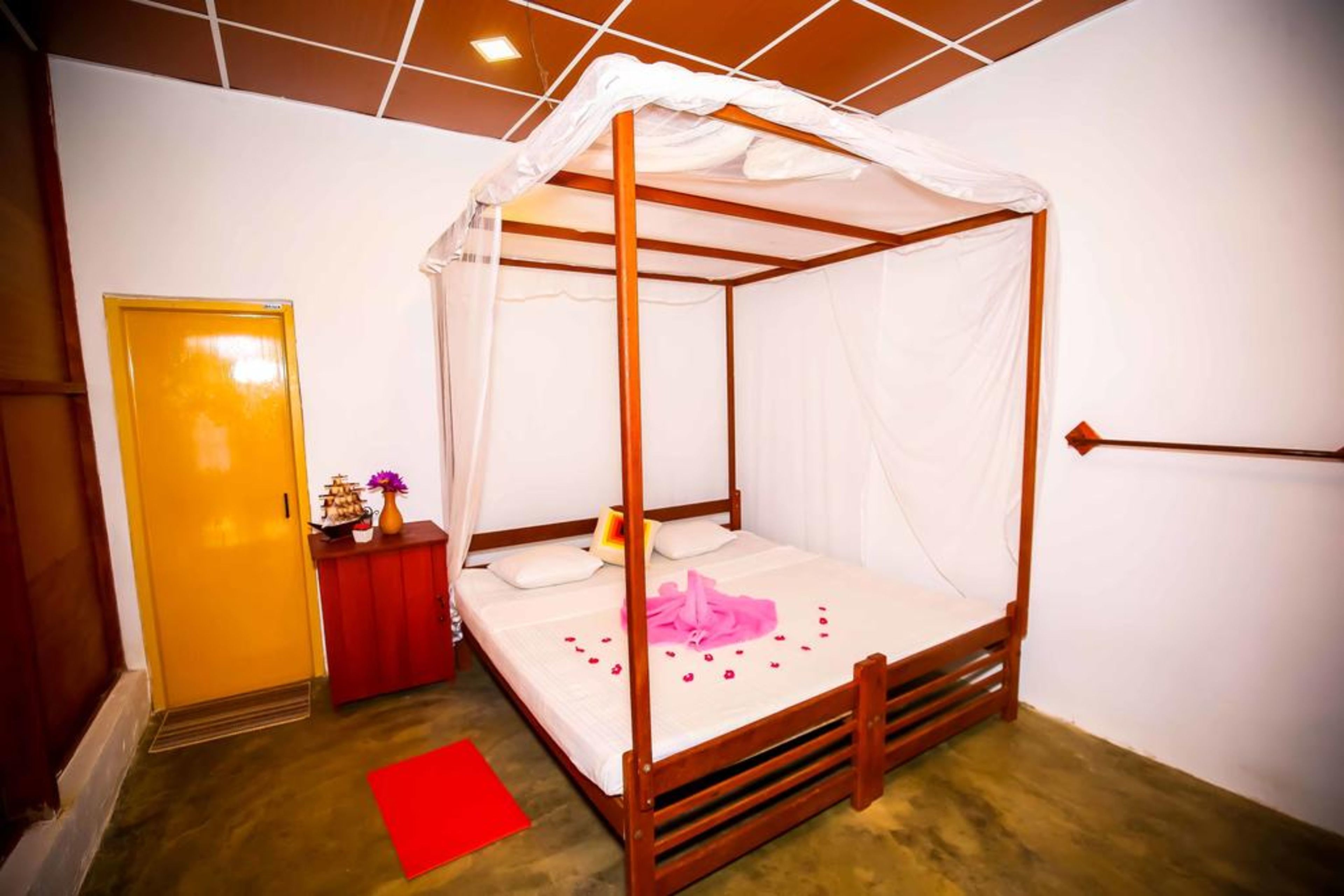 Ein Bett mit Himmelbett, ein Nachttisch in Rot mit Blumenvase und ein roter Teppich auf dem Boden.