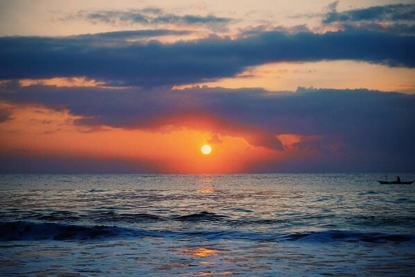 A sunset over the ocean with a boat in the distance.