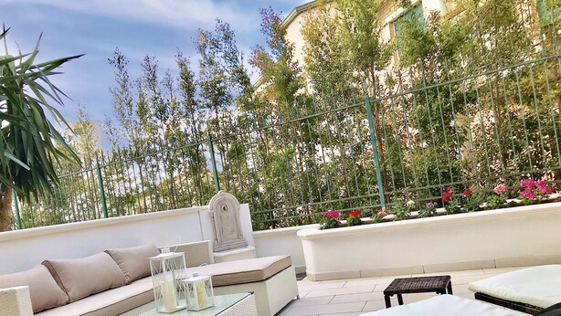 A rooftop terrace with outdoor furniture, a decorative wall, and a garden view.