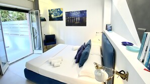 A modern bedroom with a bed, two paintings, a chair, and a view of the outdoors.