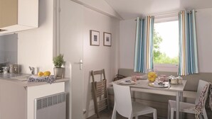 A modern kitchen with a built-in oven and a dining area with a table and chairs. - Camping des Rives des Corbieres (Leucate)