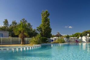 A swimming pool with clear blue water, surrounded by palm trees and a white fence. - Camping des Rives des Corbieres (Leucate)