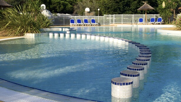 A swimming pool with blue chairs and a white fence. - Camping des Rives des Corbieres (Leucate)