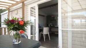 A patio area with a table, a vase of flowers, and a view into a kitchen and dining area. - Camping des Rives des Corbieres (Leucate)
