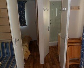 A compact room with a bed, a small wooden cabinet, and a shower area. - Camping des Rives des Corbieres (Leucate)