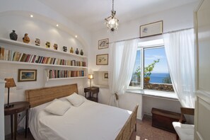 Un dormitorio con una cama, estanterías, un ventanal con vistas y un candelabro.