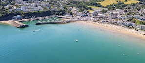 An aerial view of Sea Urchins, featuring a coastal town with a beach, marina, and surrounding greenery.