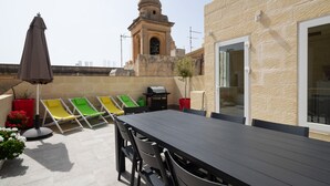 Um terraço no topo do prédio com mesa e cadeiras, churrasqueira e espreguiçadeiras coloridas.