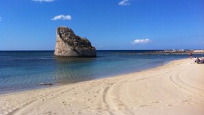 Ein Strand mit einer großen Felsformation im Wasser und einem sandigen Ufer.