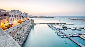 A coastal town with a historic stone wall, a marina with boats, and buildings with outdoor seating. - Stella Maris Holidays -Apartment with canopy (Torre Pali)