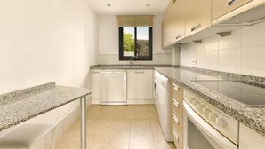 Een moderne keuken met granieten aanrechtbladen, witte kastjes, een vaatwasser, een kookplaat en een raam met uitzicht.