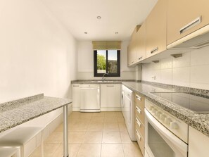 Una cocina moderna con encimeras de granito, armarios blancos, lavavajillas, estufa y ventana con vistas.