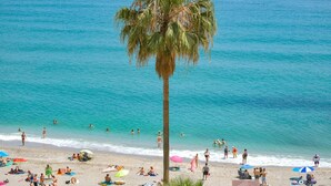 Een strand met een palmboom, mensen die zonnebaden en parasols.