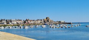 A harbor with numerous boats docked, a prominent church with a tower, and a row of residential buildings along the waterfront. - Relais des Iles  (Saint-Marcouf)