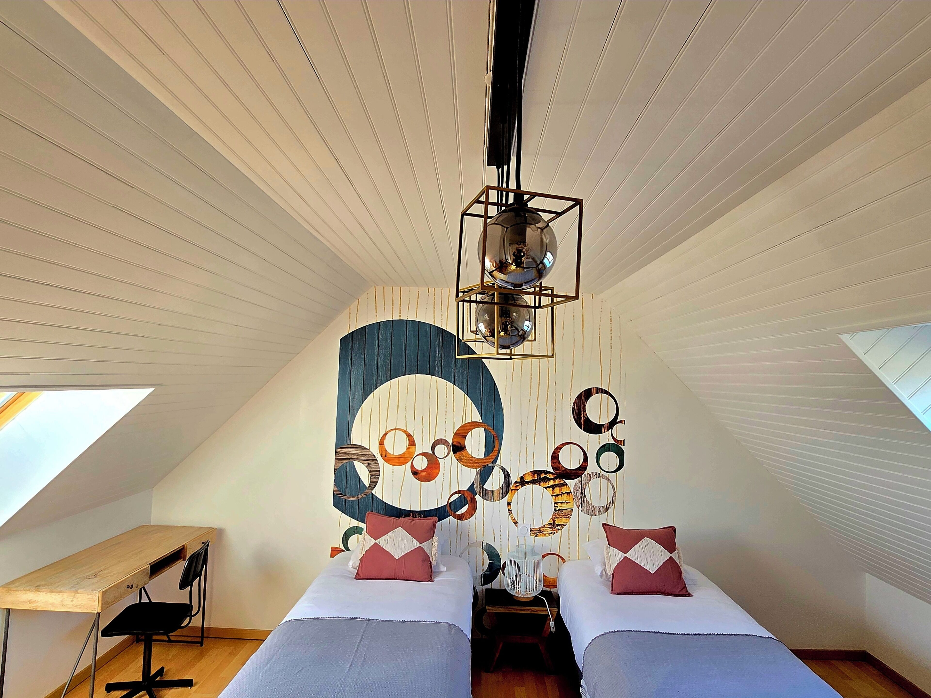 A bedroom with two beds, a desk, and a ceiling light fixture.