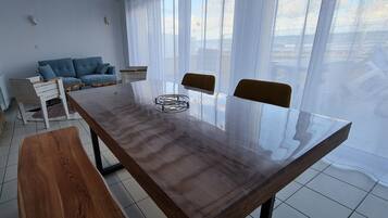 Una sala moderna con una mesa de comedor de madera, un sofá azul y un ventanal con cortinas translúcidas.