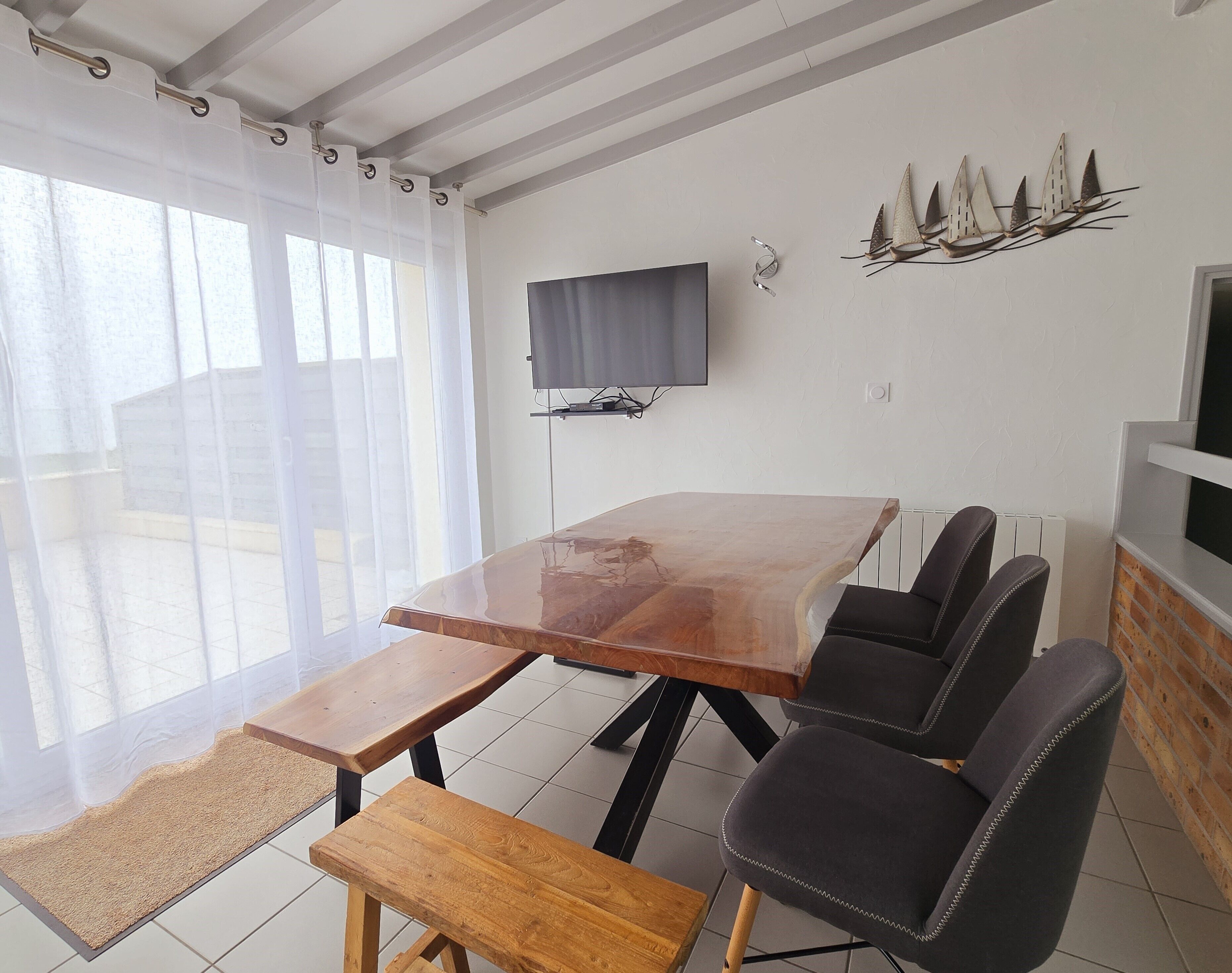 A dining area with a wooden table and chairs, a television mounted on the wall, and a decorative wall piece.