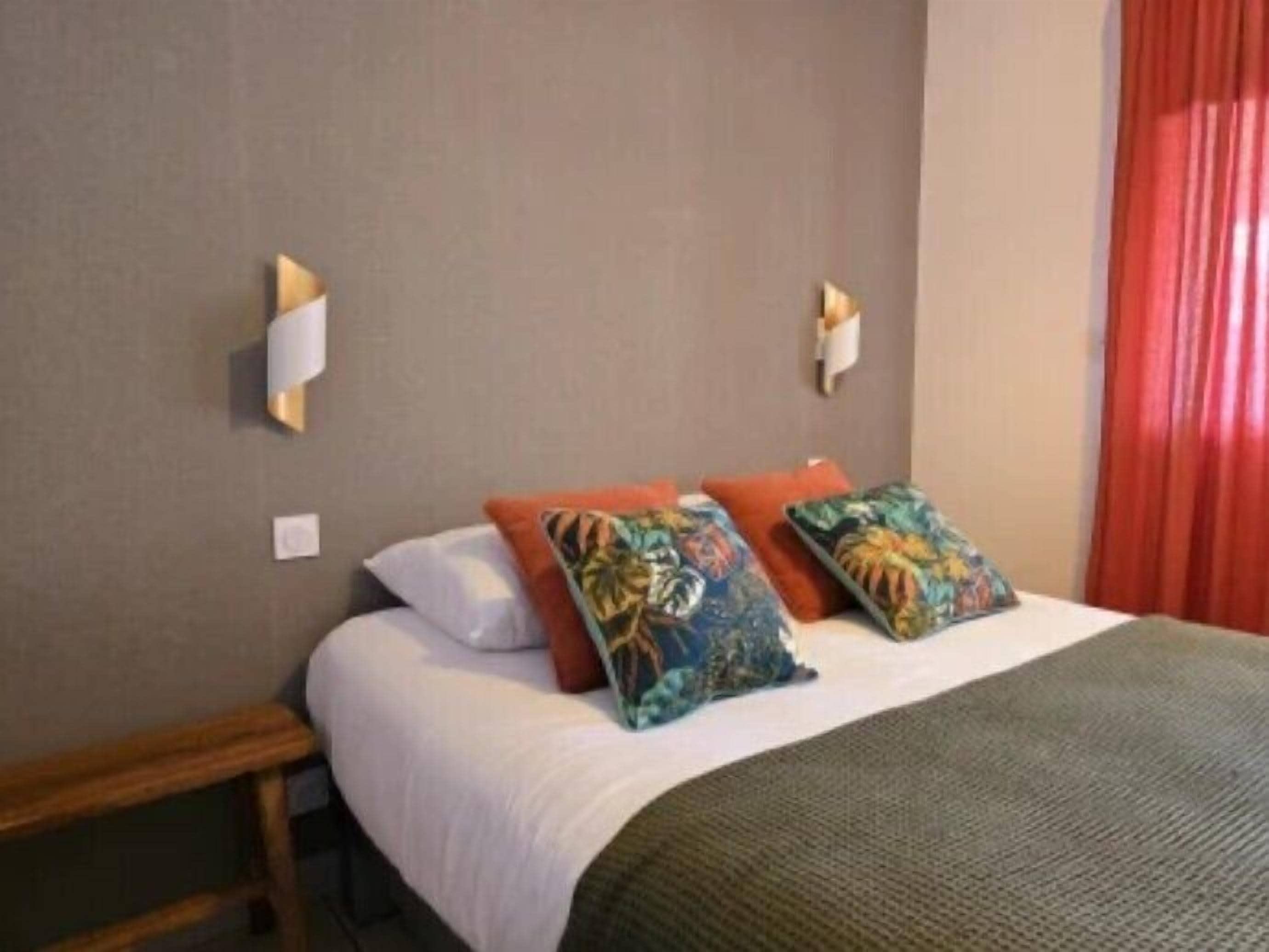 Una camera d'hotel con un letto, due cuscini, un comodino e una lampada a parete.