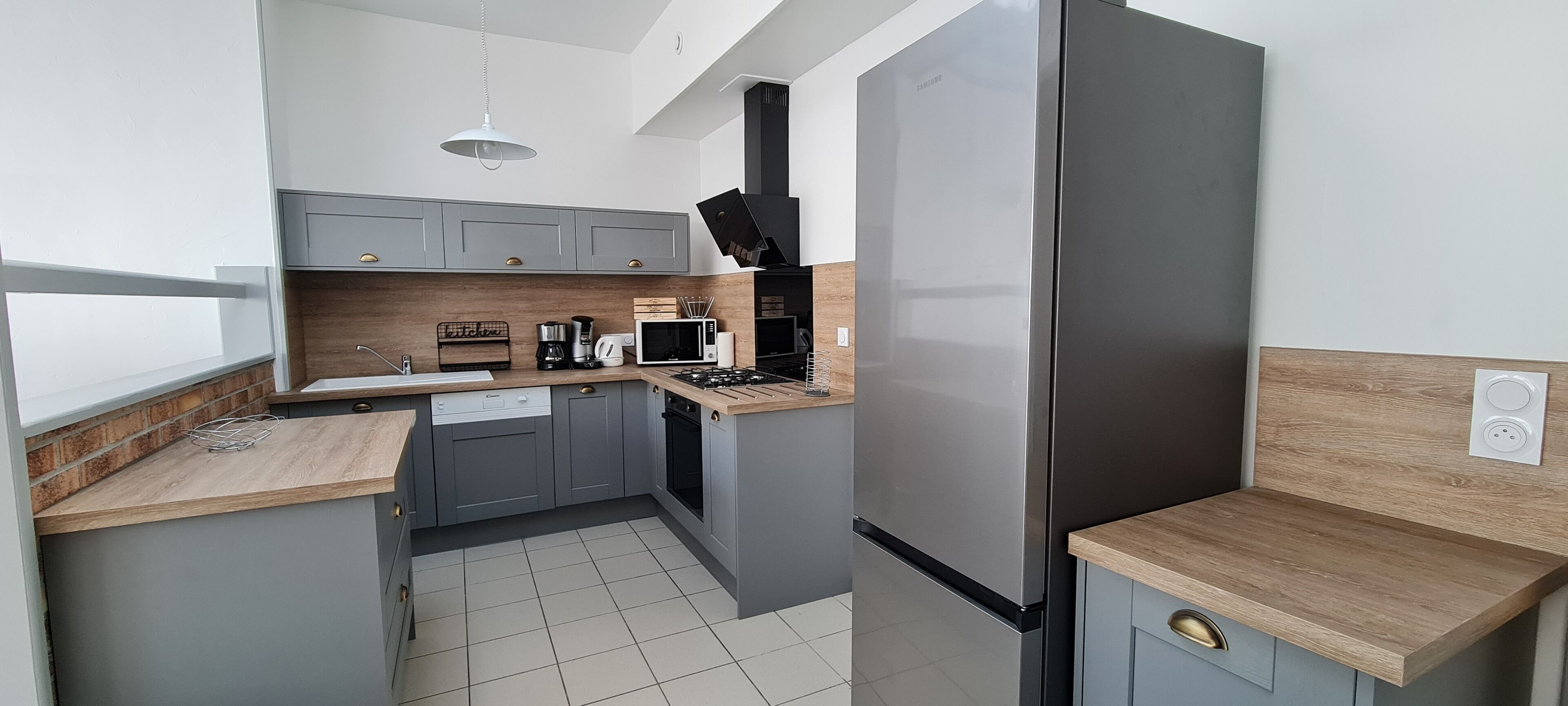 A compact kitchen with grey cabinets, a stainless steel refrigerator, a microwave, a coffee maker, and a gas stove.