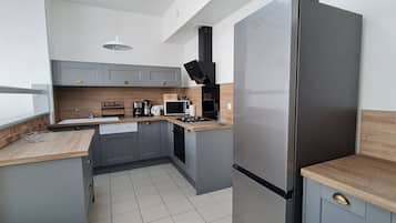 A compact kitchen with grey cabinets, a stainless steel refrigerator, a microwave, a coffee maker, and a gas stove.