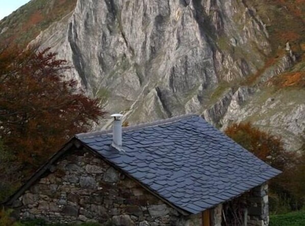 Un bâtiment en pierre doté d’un toit à forte pente, se dressant sur un fond de paysage montagneux.