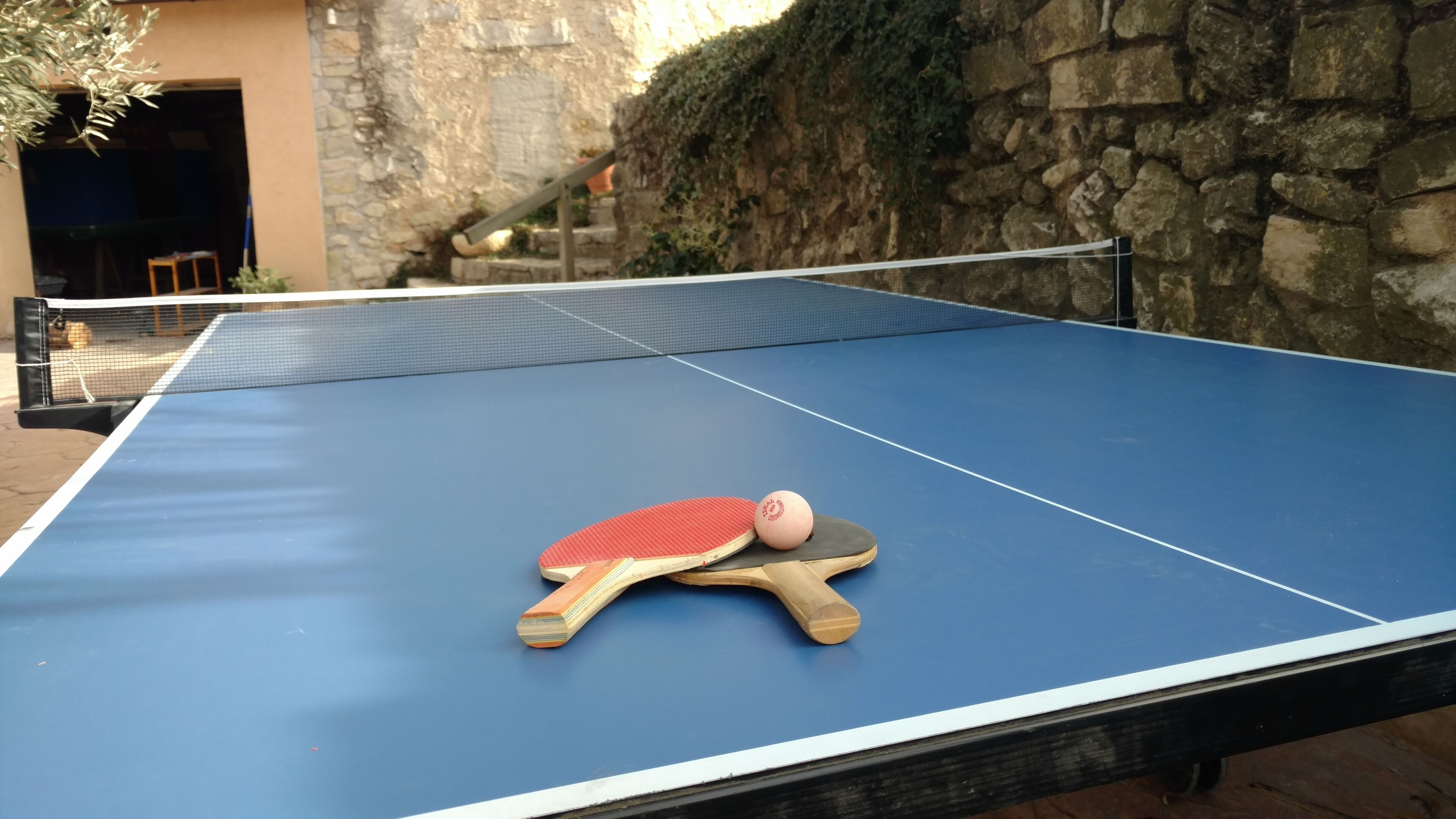 Une table de ping-pong avec des raquettes et une balle, installée en plein air.
