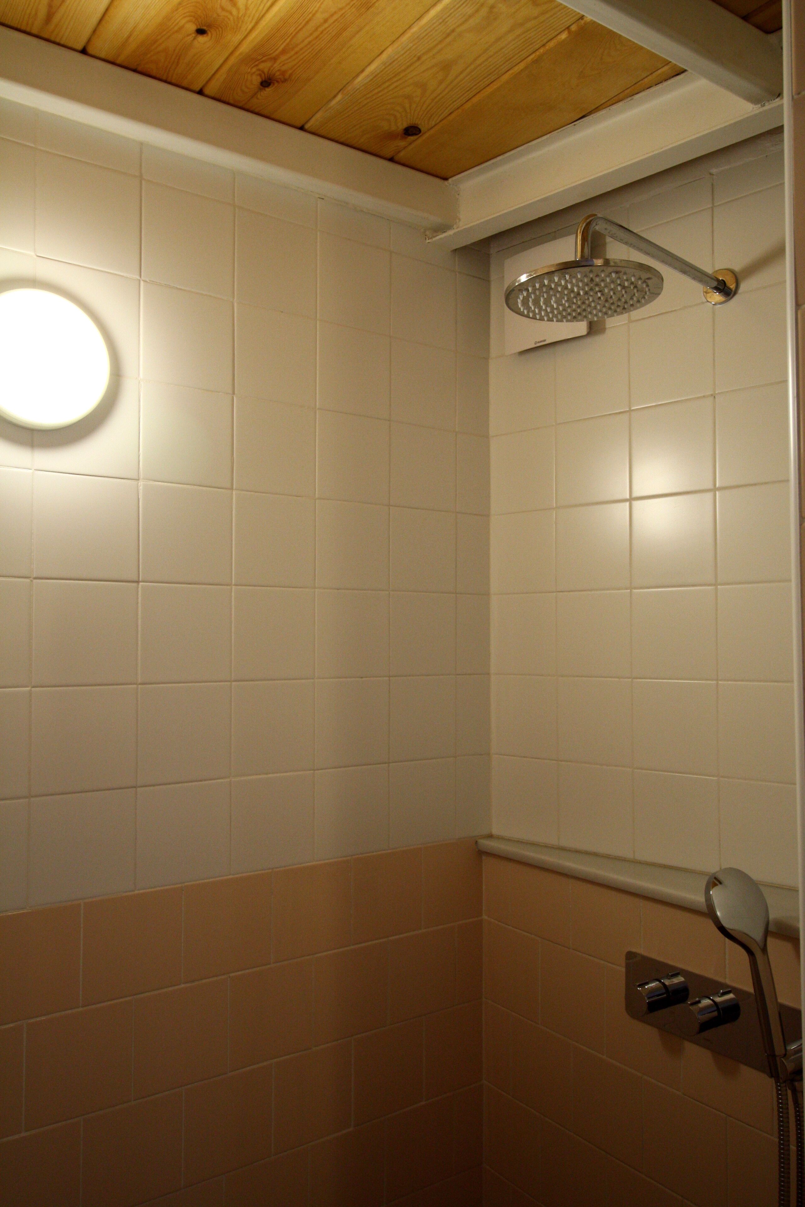 A bathroom with white and brown tiles, a showerhead, and a round light fixture.