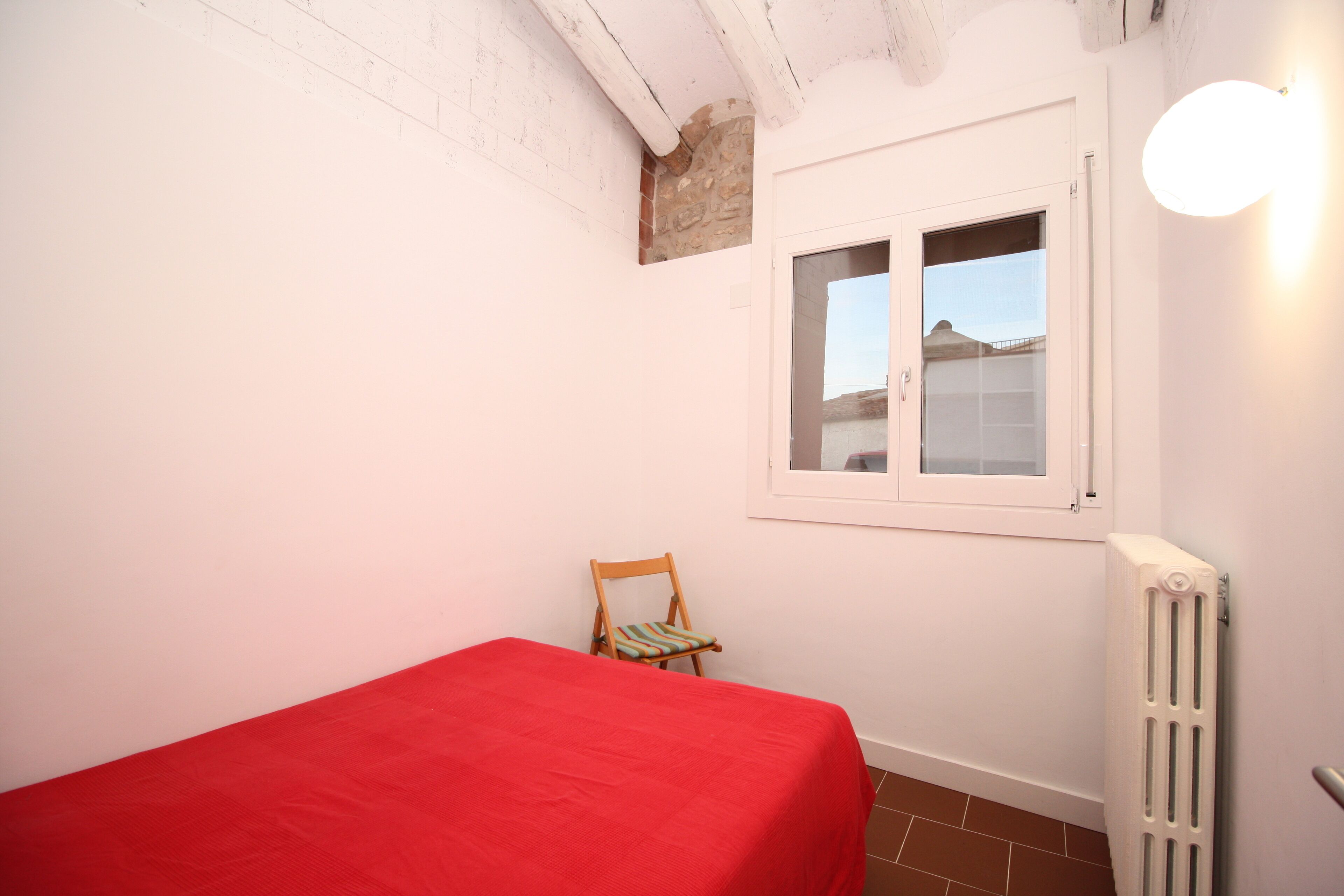Ein kleines Zimmer mit einem Einzelbett, einem Sessel, einem Fenster und einer Heizung.