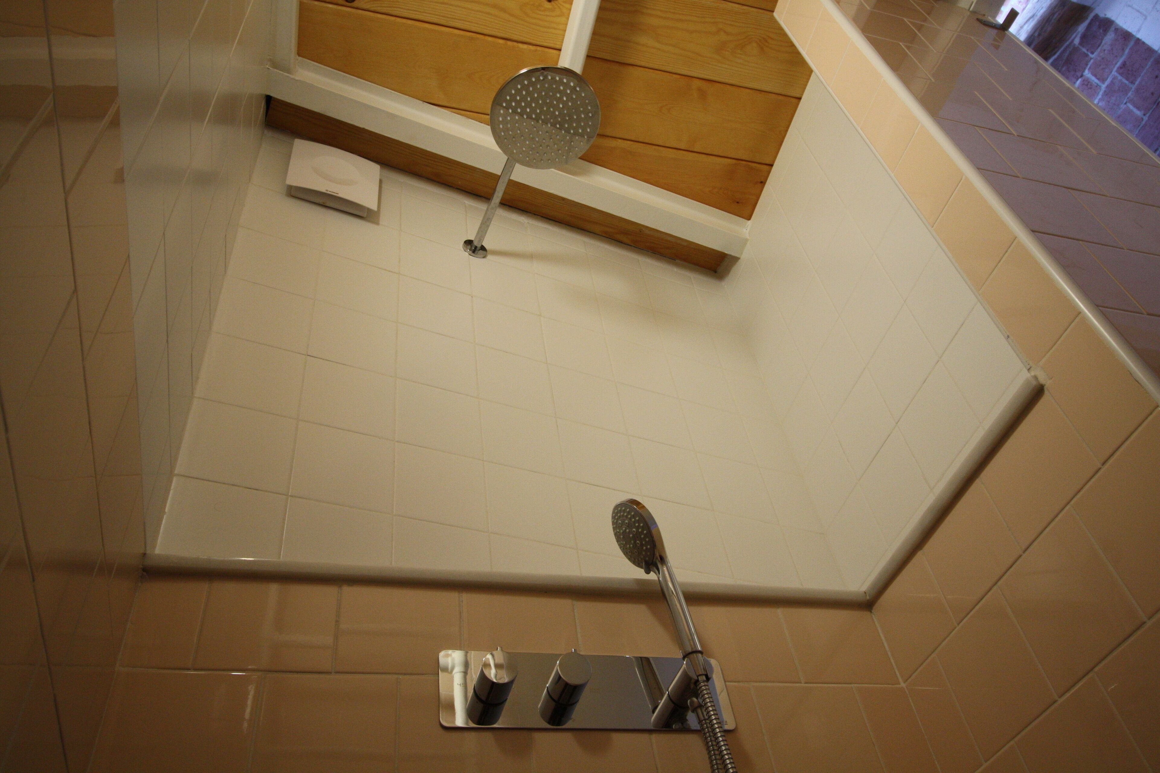A shower area with a handheld showerhead, a wall-mounted showerhead, and a mirror.
