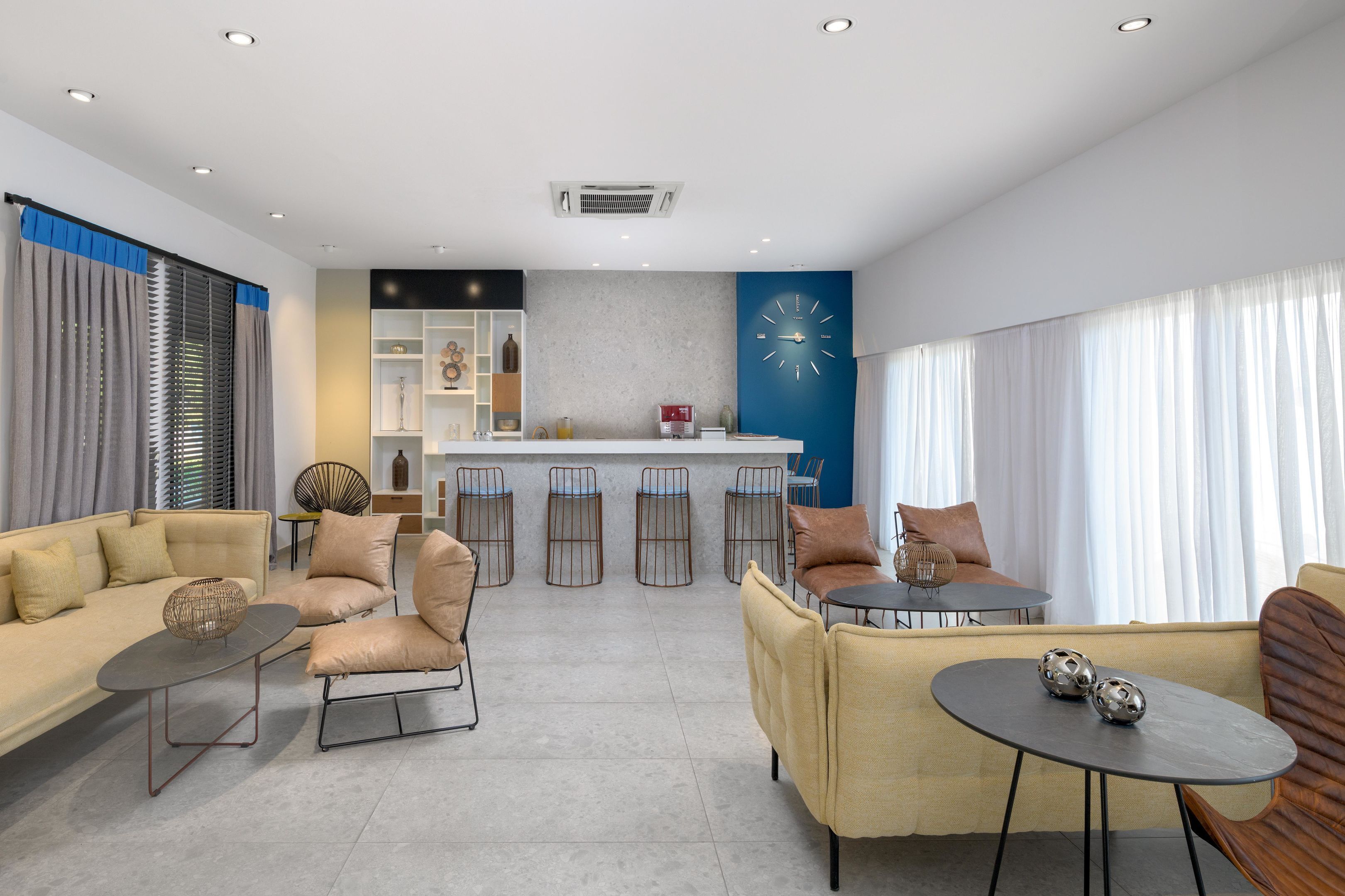Un salon moderne comprenant un canapé, des fauteuils, une table basse et un coin bar avec des tabourets.
