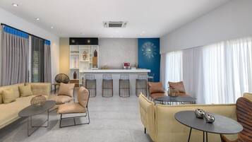 Un salon moderne comprenant un canapé, des fauteuils, une table basse et un coin bar avec des tabourets.