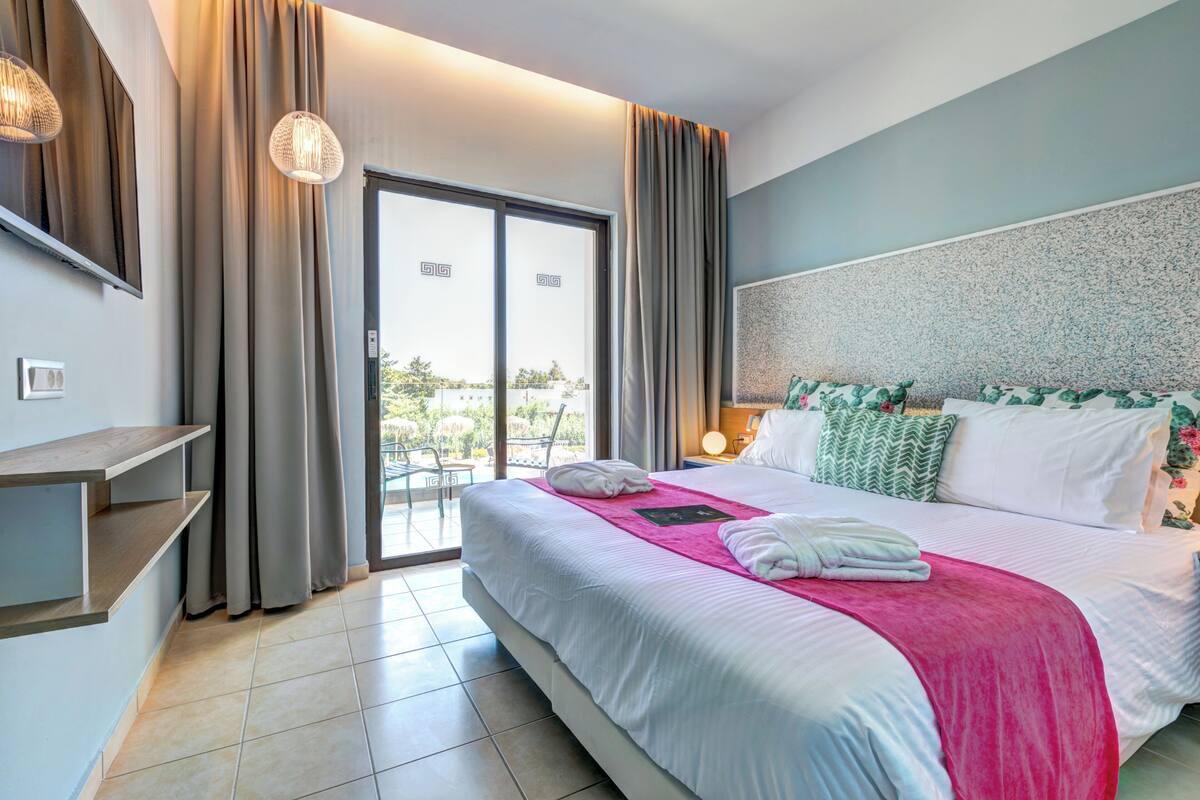 Una camera d'albergo con un letto, una scrivania, una sedia, una finestra con tende e vista sull'esterno.
